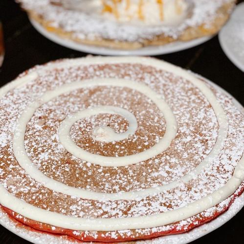 A large, round dessert topped with powdered sugar and a spiral of cream, resting on a white plate.