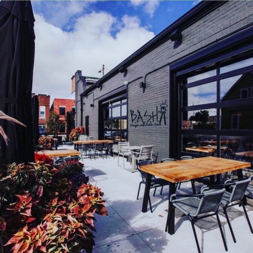 Outdoor seating area of a restaurant with wooden tables, chairs, and colorful plants under a blue sky.