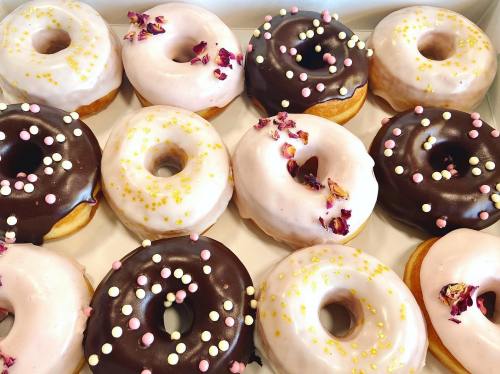 A box of assorted donuts, featuring pink and chocolate icing, sprinkles, and rose petal decorations.