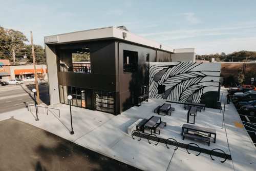 A modern building with a large mural, outdoor seating, and a clear sky in the background.