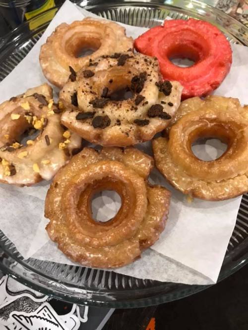 A platter of assorted donuts, including glazed, red frosted, and topped with nuts and chocolate crumbs.