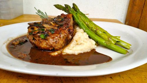 A plate featuring a pork chop with mushroom sauce, mashed potatoes, and asparagus.