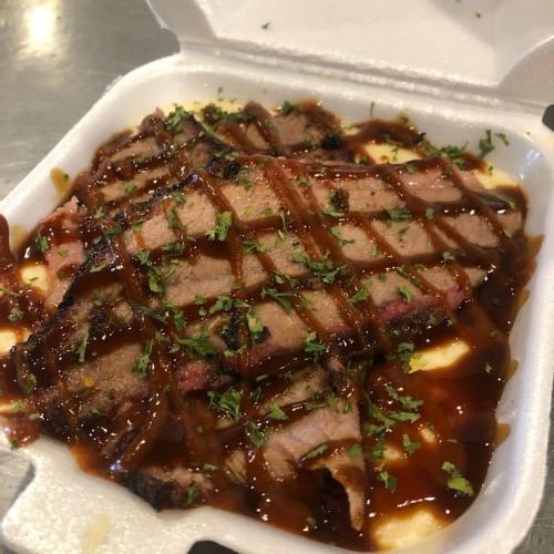 Sliced beef brisket drizzled with sauce, garnished with herbs, served in a takeout container.