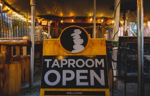 A sign reading "Taproom Open" stands in a cozy, warmly lit indoor space with wooden decor.
