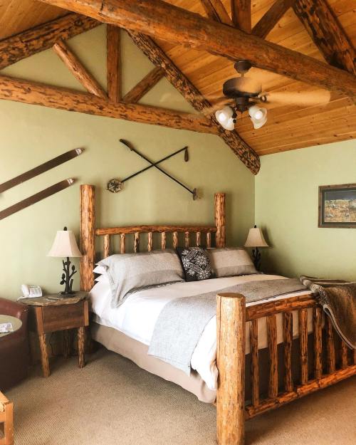 Cozy bedroom with a wooden bed, rustic decor, and a sloped ceiling featuring exposed beams and vintage skis.