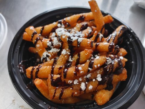 A black bowl filled with crispy, golden fries drizzled with chocolate sauce and sprinkled with powdered sugar.