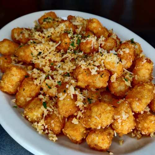 A plate of golden, crispy tater tots topped with grated cheese and parsley.
