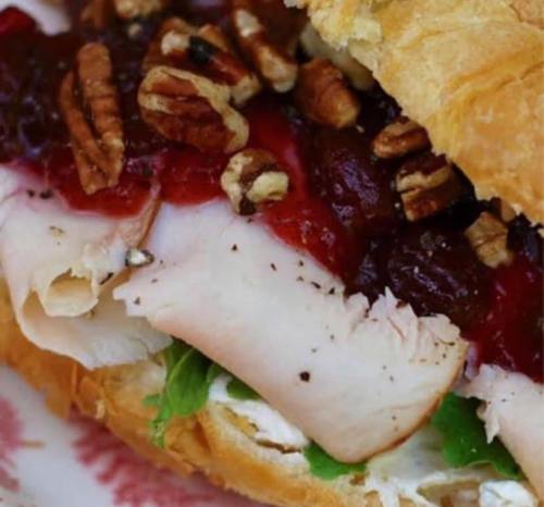 Close-up of a sandwich with turkey, cranberry sauce, pecans, and lettuce on a flaky croissant.