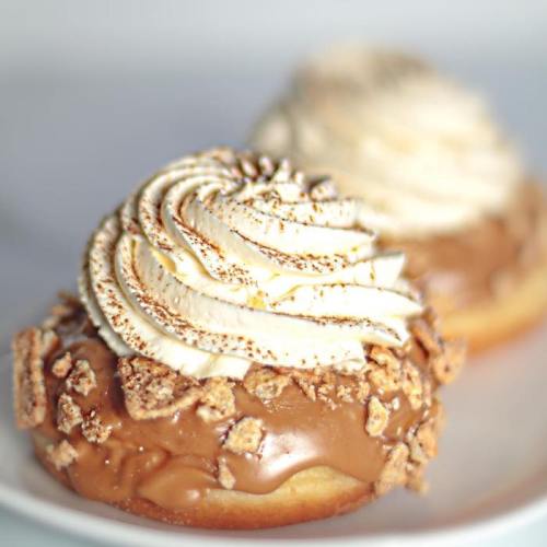 Two decadent donuts topped with swirls of whipped cream and crushed graham crackers, drizzled with caramel.