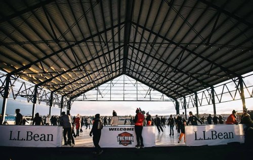 A bustling ice rink under a large roof, with skaters enjoying the space and banners for L.L. Bean displayed.