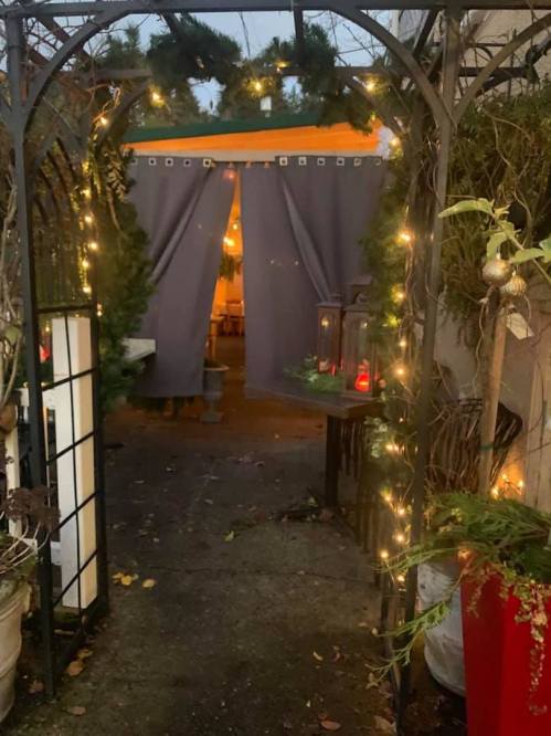 A cozy entrance adorned with greenery and fairy lights, leading to a softly lit space beyond gray curtains.