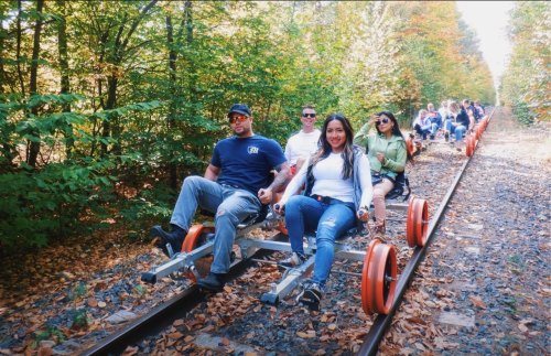 A group of people riding on a rail bike along a forested path with colorful autumn leaves.