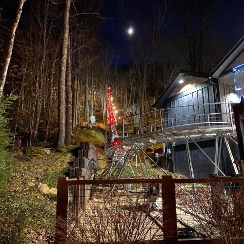A nighttime view of a roller coaster track winding through trees, with a building and moonlight in the background.