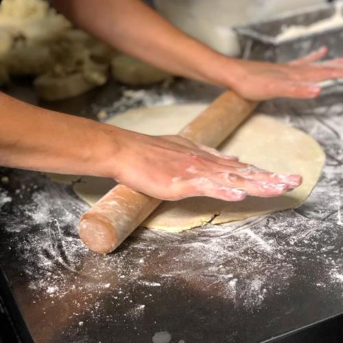 A person rolls out dough with a wooden rolling pin on a floured surface.