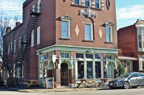 A brick building with a green trim, featuring a staircase, outdoor seating, and a sign for a restaurant.