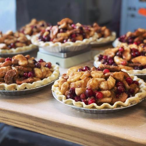 Several freshly baked fruit pies filled with apples and cranberries, arranged on a wooden table.