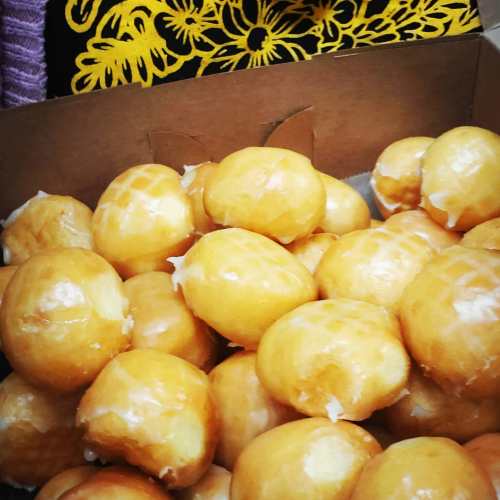 A box filled with golden, glazed doughnuts stacked closely together.
