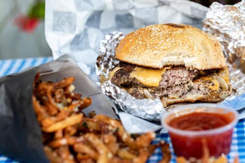 A juicy cheeseburger in a sesame seed bun, served with crispy fries and a side of ketchup on a checkered tablecloth.