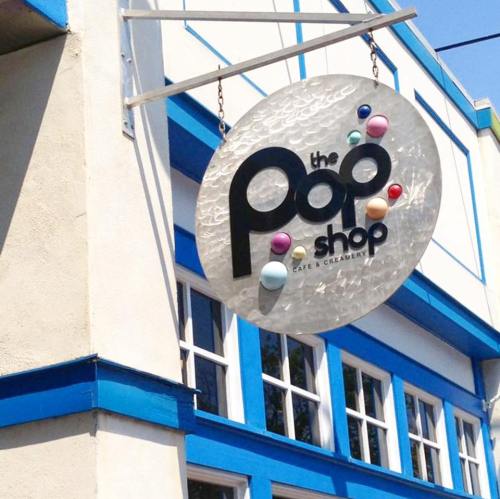 Sign for "The Pop Shop Cafe & Creamery" hanging from a building with blue trim.