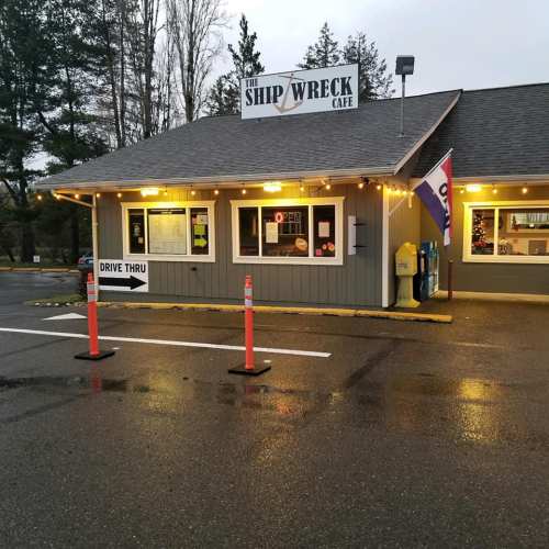 Exterior of the Ship Wreck Cafe with a drive-thru sign, illuminated at dusk, surrounded by trees.