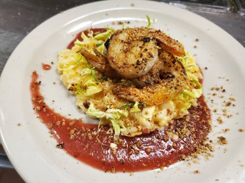 A plate of creamy risotto topped with seasoned shrimp, garnished with shredded lettuce and a drizzle of sauce.