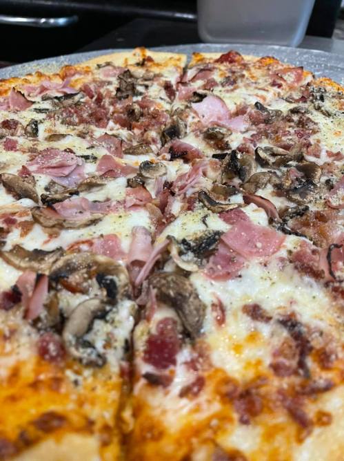 Close-up of a pizza topped with cheese, ham, mushrooms, and crispy bacon, sliced into wedges.