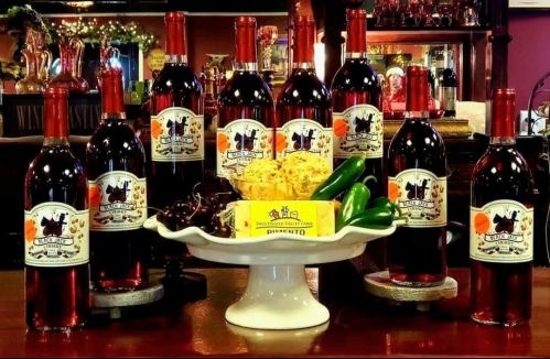 A display of wine bottles arranged around a platter with cheese, jalapeños, and cherries on a wooden table.