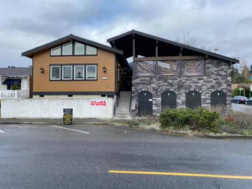 A modern building with a wooden exterior and stone accents, featuring large windows and a covered patio area.