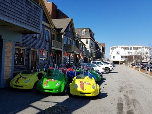 Colorful go-karts lined up on a sunny street in front of charming buildings.