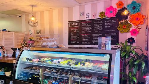 A cozy café display with a glass case of desserts, a menu board, and colorful paper flowers on the wall.