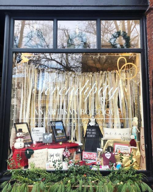 A boutique window display featuring festive decorations, accessories, and signs with messages of home and joy.