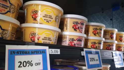 Shelves displaying various tubs of cold pack cheese spread with price tags and a sign for an in-store special.