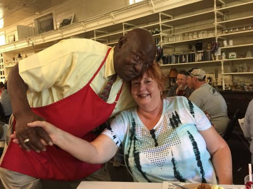 A smiling man in an apron poses with a woman at a restaurant, both enjoying a friendly moment together.
