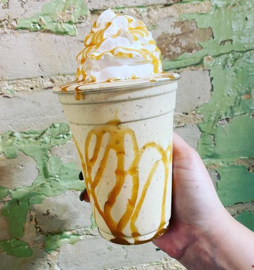 A hand holding a tall cup of caramel milkshake topped with whipped cream and drizzled with caramel sauce.