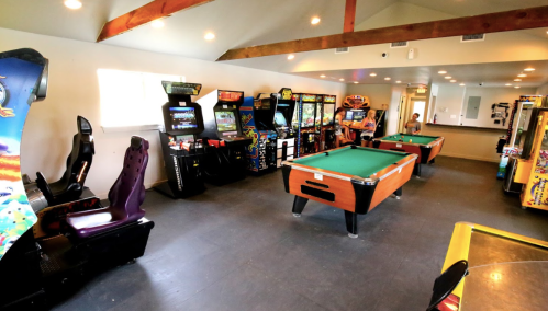 A game room featuring arcade machines, a pool table, and a cozy atmosphere with wooden beams.