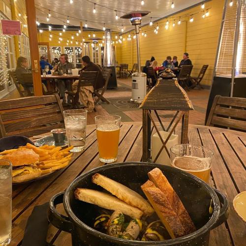 A cozy outdoor dining scene with a pot of food, drinks, and people enjoying a meal under string lights.