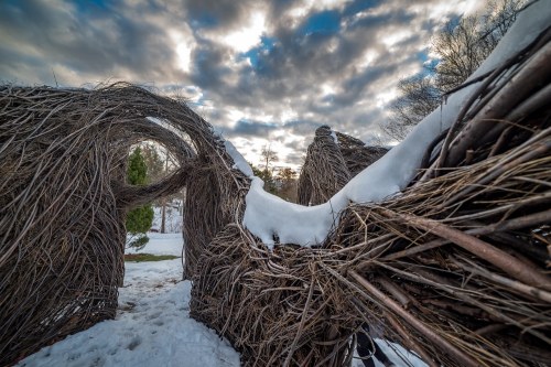 A snowy landscape featuring a woven structure with arches, under a cloudy sky.