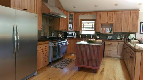 A modern kitchen with wooden cabinets, stainless steel appliances, and a central island with a fruit bowl.