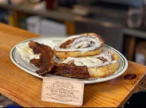 A plate with cinnamon rolls drizzled with icing and crispy bacon, alongside a business card for Berry Fields Cafe.