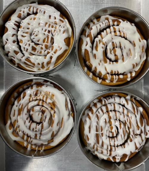 Four round pans filled with freshly baked cinnamon rolls drizzled with white icing, arranged in a grid.