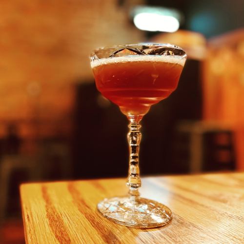 A cocktail in an elegant glass sits on a wooden table, with a blurred background of a cozy bar setting.