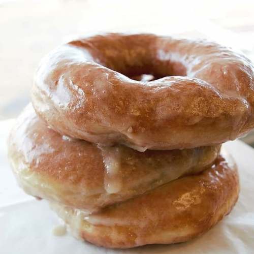 Three glazed donuts stacked on top of each other, showcasing a shiny, golden-brown exterior.