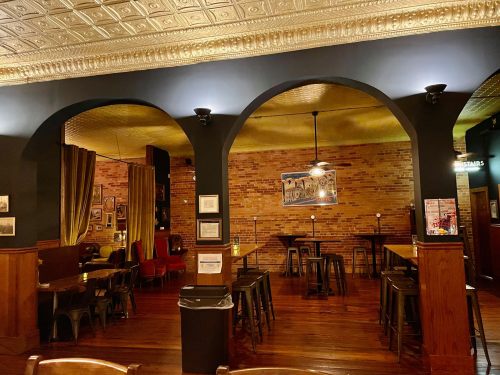 Interior of a cozy restaurant featuring brick walls, wooden tables, and arched doorways with warm lighting.