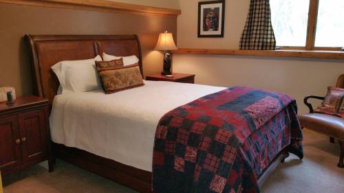 Cozy bedroom featuring a wooden bed, quilted blanket, bedside lamp, and a window with checkered curtains.