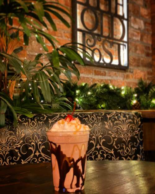 A delicious milkshake topped with whipped cream and a cherry, set against a cozy, brick-walled café backdrop.