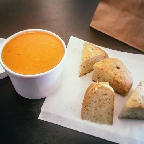 A cup of orange soup next to three pieces of bread on a white napkin.