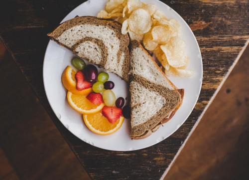 A plate with a sandwich, potato chips, and a side of orange slices, strawberries, grapes, and other fruits.
