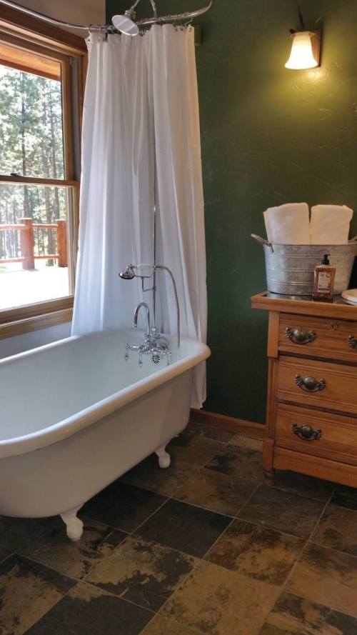 A cozy bathroom featuring a vintage clawfoot tub, a white shower curtain, and a wooden dresser with towels and toiletries.