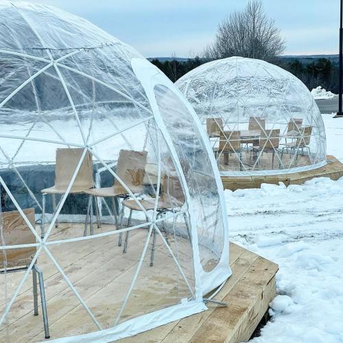 Two transparent geodesic domes on a snowy landscape, each with wooden platforms and chairs inside.