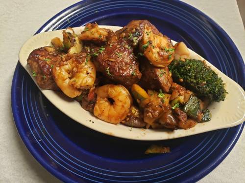 A vibrant dish featuring shrimp, beef, and mixed vegetables on a blue plate, garnished with herbs.